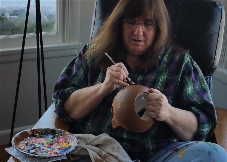 Strawn 60, paints baby helmets from the living room of her Washington home.