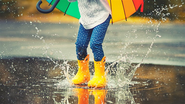 Fötter of child in yellow rubber boots jumping over puddle in rain