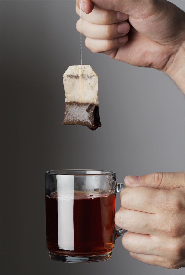 Mână lifting a used tea bag from a glass tea mug.